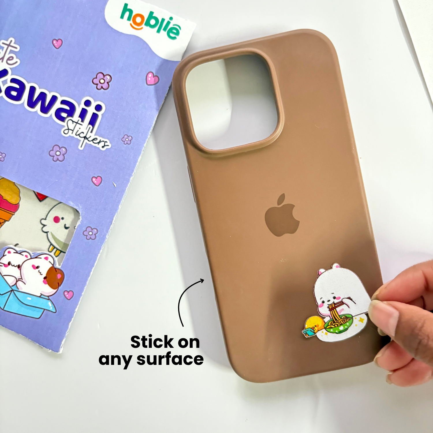 Brown phone case with a sticker being applied, next to a pack of stickers.