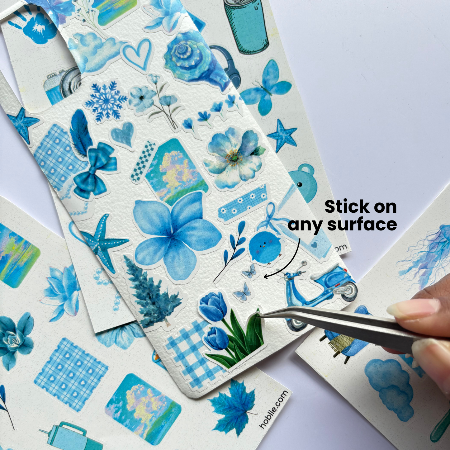 Sheet of blue floral and patterned stickers with a hand using tweezers to pick up a sticker.