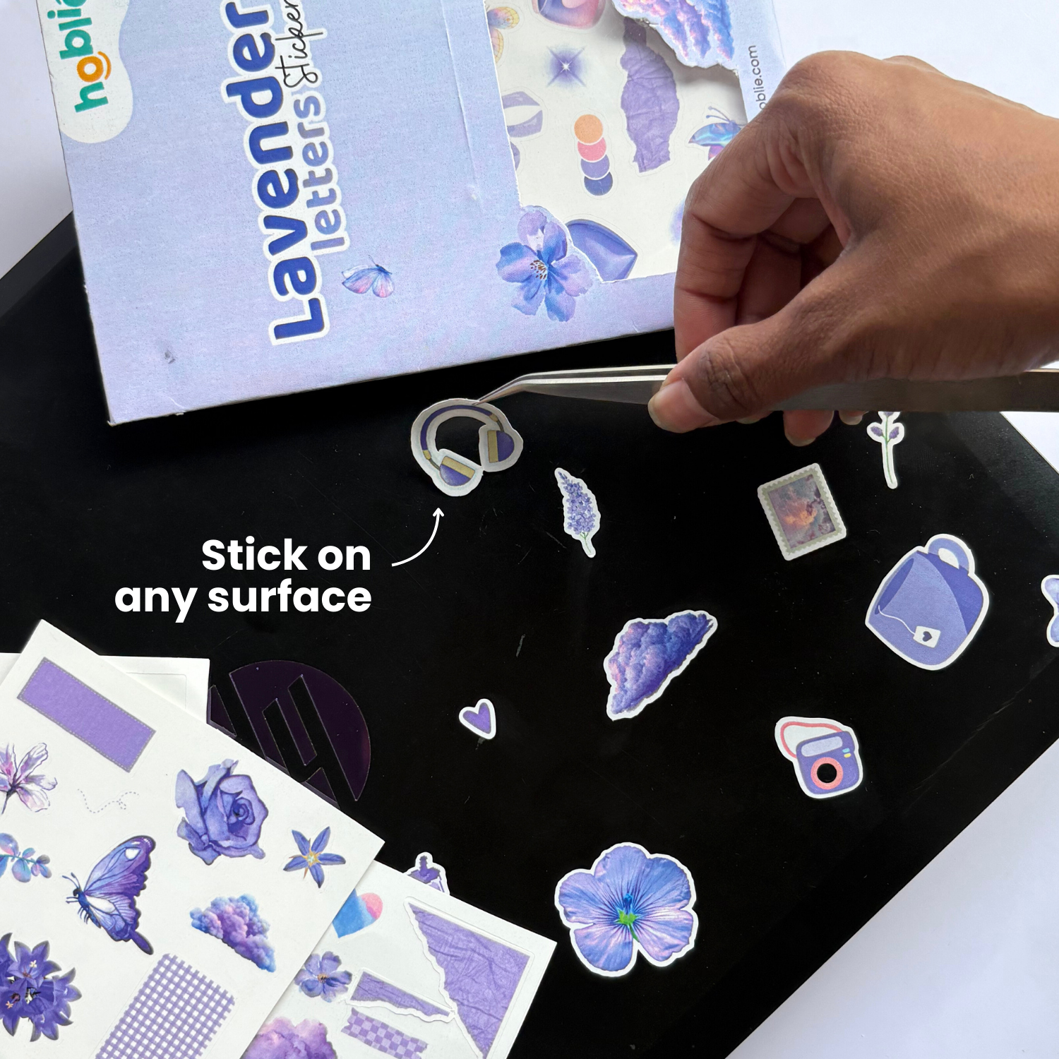 Hand applying lavender-themed stickers on a black surface with 'Hobby' branding visible.